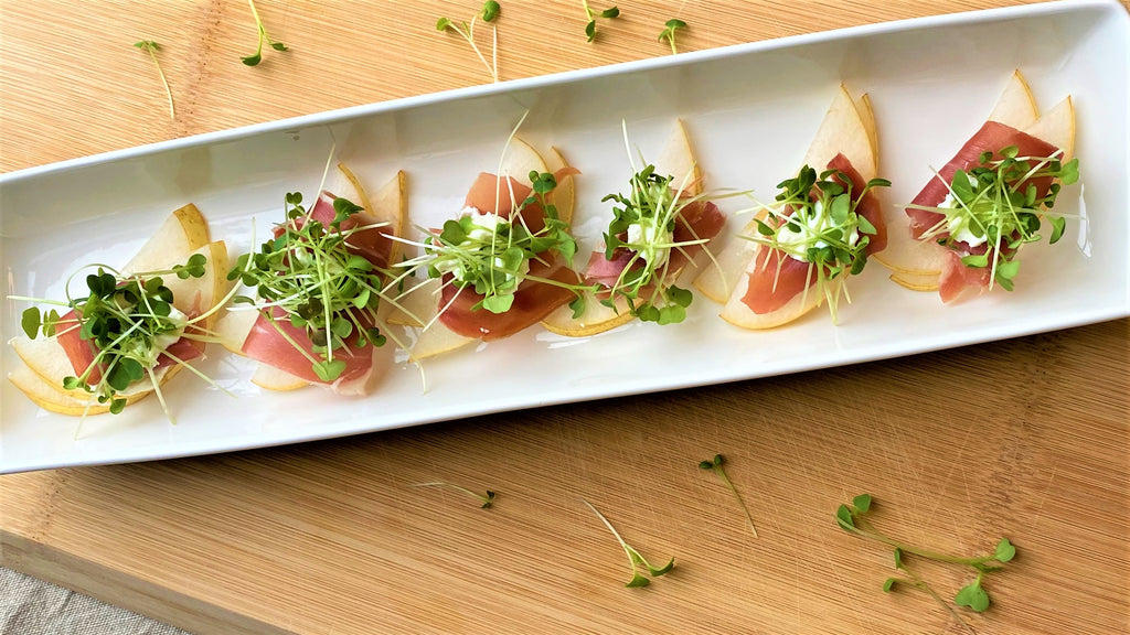 Pear and prosciutto appetizers lined up on a plate with microgreens on top